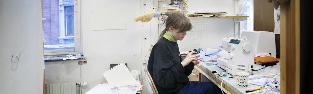 Kvinnlig student sitter och arbetar med sitt verk vid ett arbetsbord.