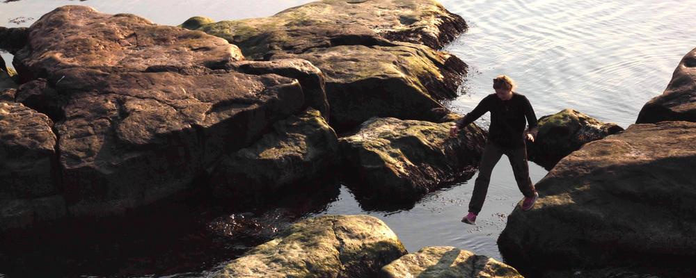 Girl with black clothes and pink sneakers walking on rocks by the sea