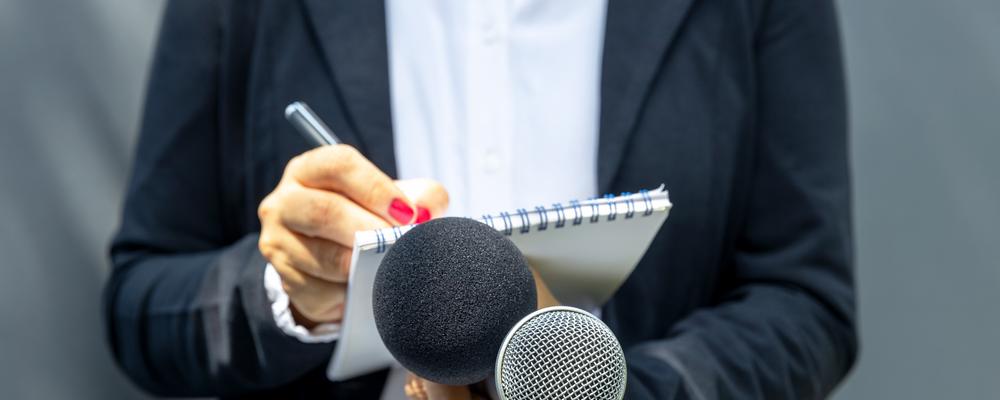 Bild på journalist som skriver och håller upp mikrofoner
