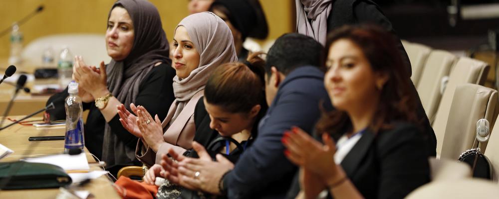  A group of women and men are participating and applauding during a meeting or conference. They look engaged and attentive