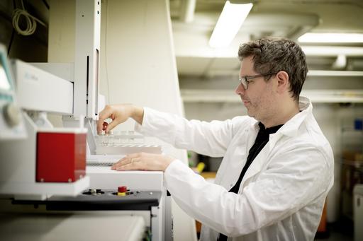 En man i en vit rock står i ett labb med ett vattenprov. 